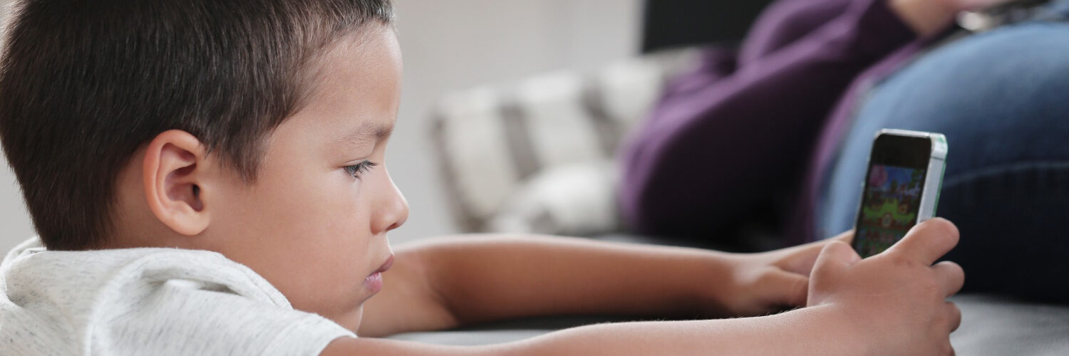 bambino con un dispositivo digitale e genitore sullo sfondo