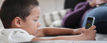 bambino con un dispositivo digitale e genitore sullo sfondo