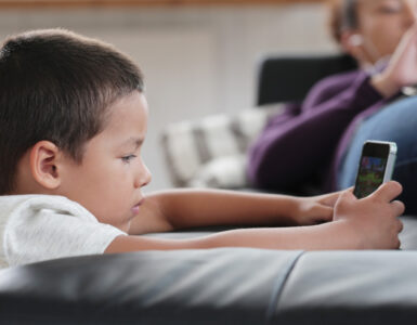 bambino con un dispositivo digitale e genitore sullo sfondo