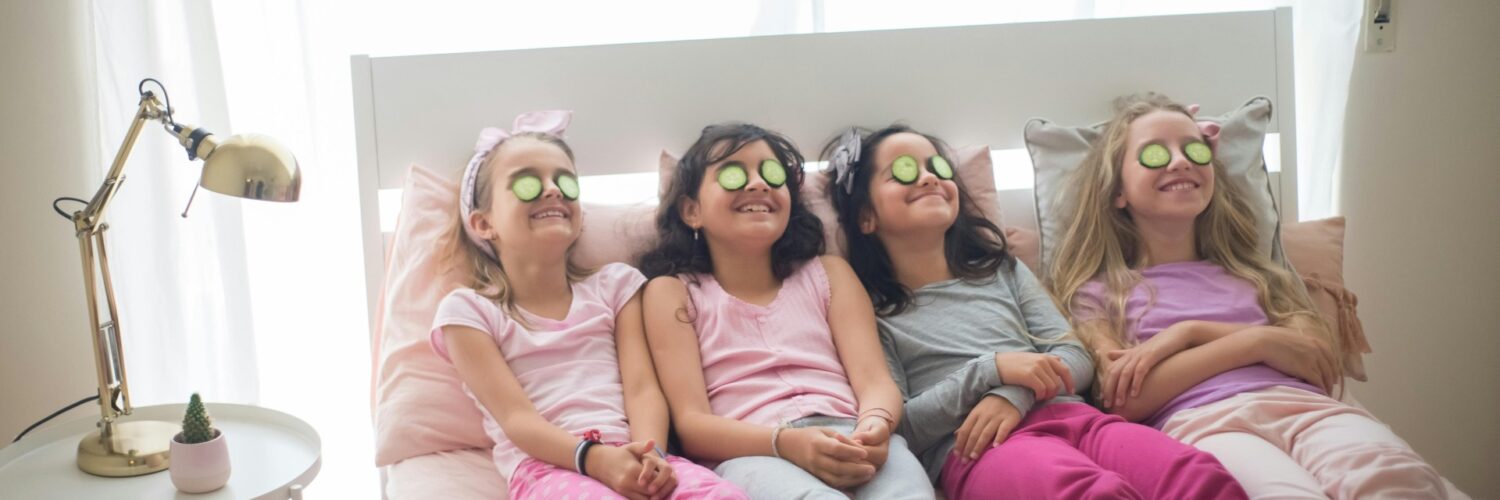 Quattro bambine in pigiama con fette di cetrioli sugli occhi sedute sul letto