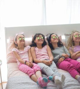 Quattro bambine in pigiama con fette di cetrioli sugli occhi sedute sul letto
