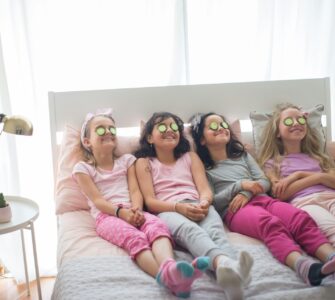Quattro bambine in pigiama con fette di cetrioli sugli occhi sedute sul letto